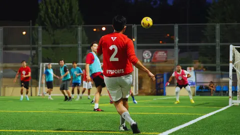 Jugador chutando balón en partido de fútbol amateur en campo iluminado